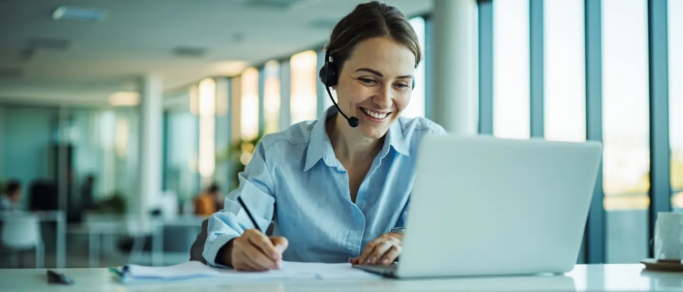 A recruiter on a headset call, taking notes on a search